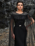 Luxury black beaded mermaid evening gown featuring a glamorous sheer tulle cape, intricate crystal fringe detailing on the neckline, and sparkling long sleeves for formal galas or red carpets.