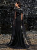 Luxury black beaded mermaid evening gown featuring a glamorous sheer tulle cape, intricate crystal fringe detailing on the neckline, and sparkling long sleeves for formal galas or red carpets.