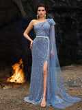 Luxury royal blue beaded mermaid evening gown featuring an elegant asymmetrical neckline, a high thigh slit, and a dramatic sheer flowing cape shawl for formal galas or red carpets.
