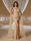 Woman in a champagne gold evening gown with floor-length sheer cape sleeves and crystal embroidery, featuring a high slit design in an elegant ballroom setting.
