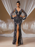 A woman wearing an elegant black chiffon mermaid evening gown with a deep V-neck, featuring intricate crystal beading, long sheer sleeves, and a high thigh slit, standing in front of white chandeliers.