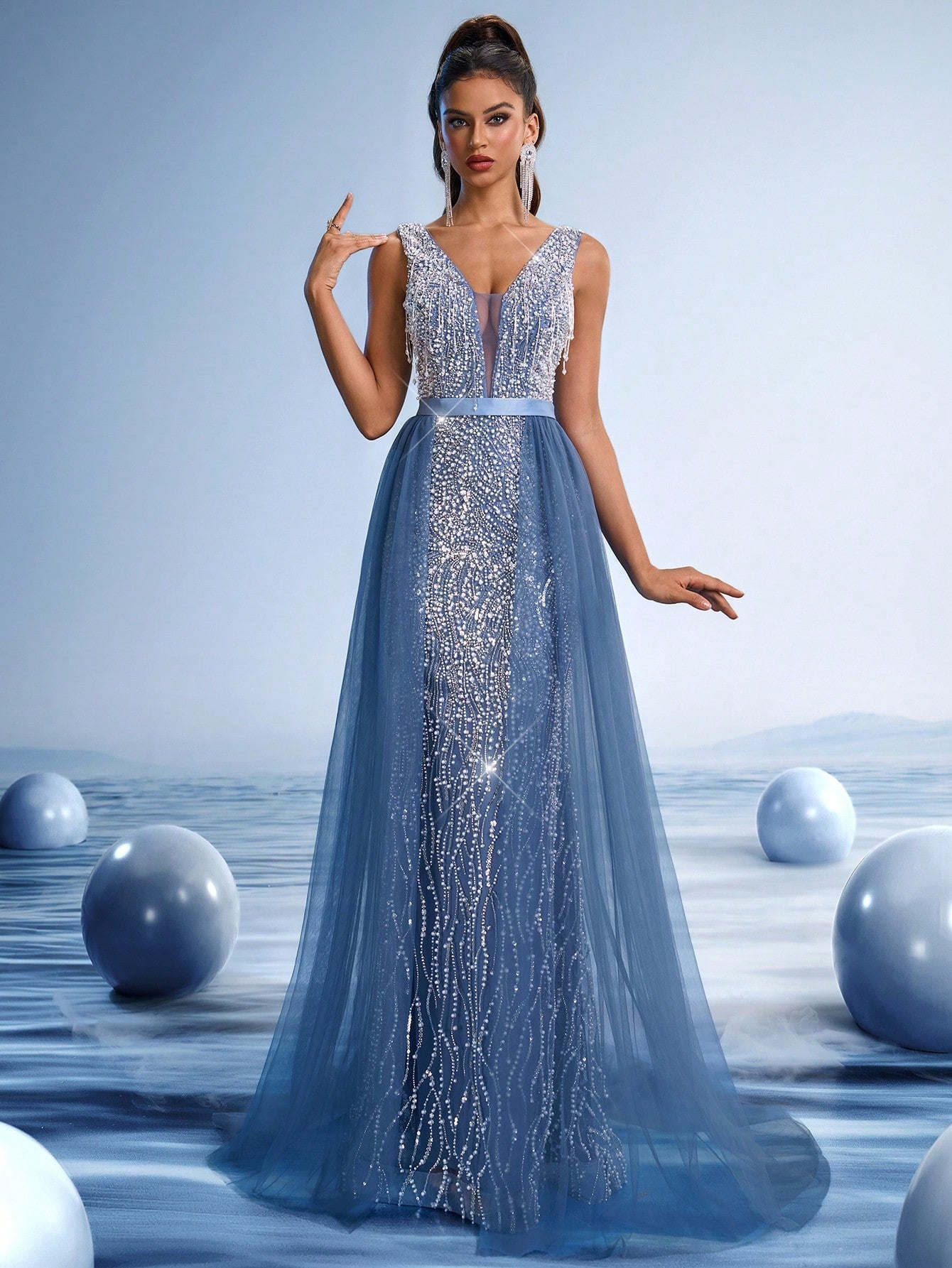 Woman wearing a royal blue crystal beaded evening gown with a deep V-neck and sheer bodice, posing against a futuristic blue background.