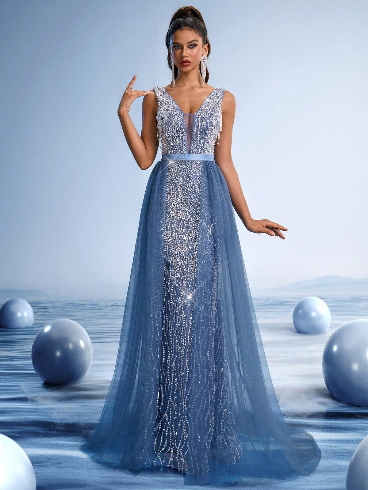 Woman wearing a royal blue crystal beaded evening gown with a deep V-neck and sheer bodice, posing against a futuristic blue background.