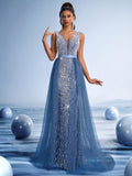 Woman wearing a royal blue crystal beaded evening gown with a deep V-neck and sheer bodice, posing against a futuristic blue background.