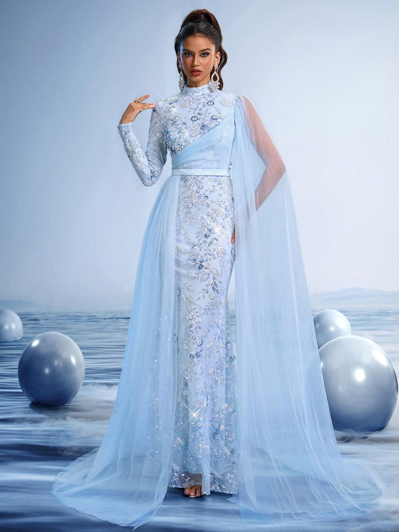 Ethereal sky blue evening gown featuring intricate crystal floral embroidery, an elegant off-shoulder neckline, and a dramatic flowing sheer tulle cape for luxury weddings or galas.