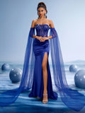 Elegant woman wearing a royal blue off-shoulder evening gown with intricate beaded bodice, high thigh slit, and a dramatic floor-length sheer chiffon cape.