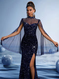 Woman wearing a sparkling navy blue evening gown featuring a high neck illusion mesh bodice with delicate beading, dramatic sheer cape sleeves, and a high thigh slit against a soft blue background.